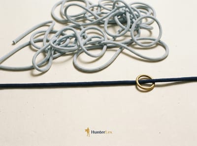A loosely tangled pale cord above a single straight navy cord threaded with a brass ring